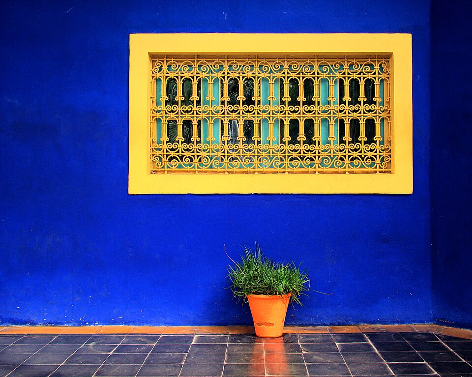 A yellow decorative window and orange planter against a cobalt-blue wall at Jardin Majorelle
